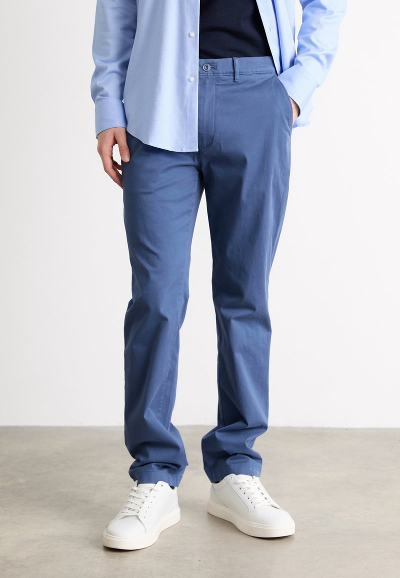 Ljusblå bomullshängselbyxor med rak passform och sidofickor, i kombination med vita sneakers. Slät textur, utan synliga mönster eller accenter.