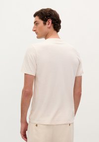 Maglietta beige chiaro con maniche corte, collo rotondo e vestibilità rilassata. Materiale in cotone morbido; design minimalista senza motivi visibili.