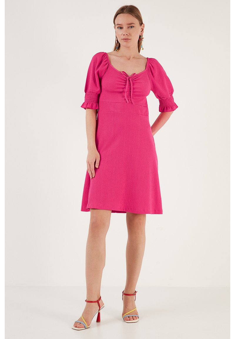Pink, short-sleeved dress with a fitted bodice and flared skirt. Textured fabric and tie detail at the neckline.
