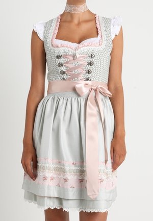 Kvinde iført en traditionel lysegrå dirndl kjole med lyserødt bånd, lyserødt bånd i taljen, blomster- og blonderforklæde samt en hvid blondechoker.