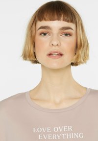 Blush-pink T-Shirt mit kurzen Ärmeln und dem weißen Aufdruck "LOVE OVER EVERYTHING". Weicher Stoff und runder Ausschnitt. Minimalistisches Design.