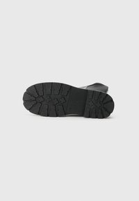 Semelle de chaussure en caoutchouc noir avec une surface texturée, dotée de profondes rainures et d'un design robuste pour une meilleure adhérence et durabilité.