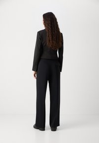 Black fitted blazer with structured shoulders, paired with high-waisted black wide-leg trousers. Smooth texture, minimal hardware, and a subtle label accent.