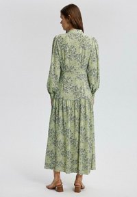 Rochie maxi cu imprimeu floral verde, cu mâneci lungi și bufante, tiv stratificat și guler înalt. Purtați cu sandale cu toc bloc maro.