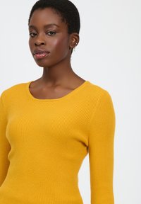 Maglione a coste in giallo senape, con scollo rotondo e maniche lunghe, realizzato in un tessuto morbido e testurizzato.