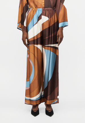 Bukser med vide ben og elastisk talje med abstrakte brune, blå, hvide og sorte buede mønstre, båret med sorte spidse sko.