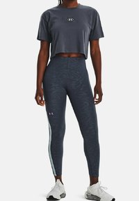 Mörkgrå, kortärmad t-shirt med en broderad logotyp, i kombination med högmidjade leggings med mönstrad textur och ljus sidränna.