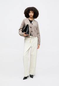 Šviesiai rudas megztinis su mygtukais, baltos plačios kelnės ir juodi aukštakulniai bateliai. Laikoma juoda trikampė rankinė.