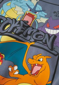 Maglietta grafica con personaggi dei Pokémon in stile cartoon: Gyarados, Charizard, Gengar, e un logo "Pokémon" nero su uno sfondo grigio.