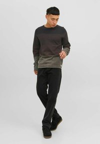 Langdurige sweater met lange mouwen in een verloop van donkergrijs naar lichtgrijs, gecombineerd met zwarte broek en zwarte schoenen met een gestructureerde zool.