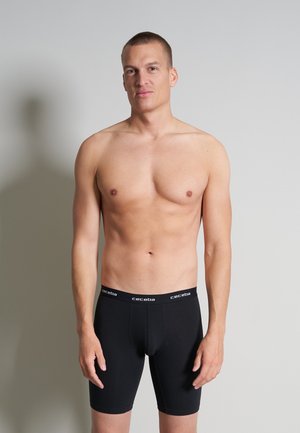 Zwarte katoenen boxers met een snug fit; merkband met "ceceba" in het wit; model is shirtloos en staat voor een neutrale achtergrond.