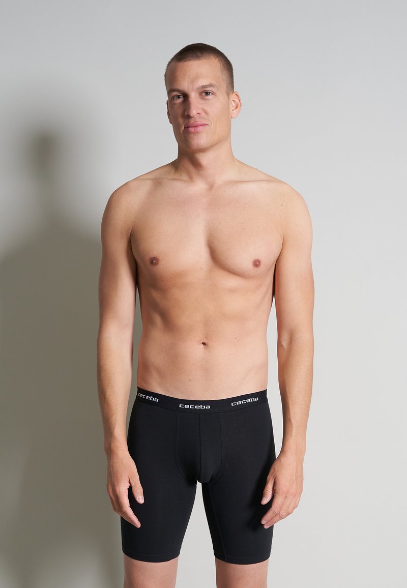 Boxers en coton noir avec une coupe ajustée ; ceinture de marque avec "ceceba" en blanc ; le modèle est torse nu, affichant un fond neutre.