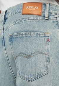 Ανοιχτό μπλε ντένιμ παντελόνια με δερμάτινη ετικέτα με την ένδειξη "REPLAY" στη μέση, ορατή πίσω τσέπη με κόκκινες λεπτομέρειες ραφής.