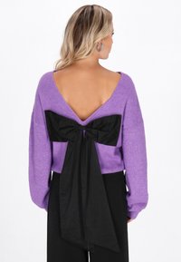 Paarse gebreide sweater met een diepe V-rug en een grote zwarte stoffen strikdetail op de onderrug. Casual pasvorm met lange mouwen.