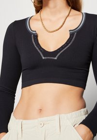 Černý zvlněný crop top s hlubokým, zaobleným výstřihem a šedými akcenty a dlouhými rukávy. Výrazné šití kolem výstřihu.