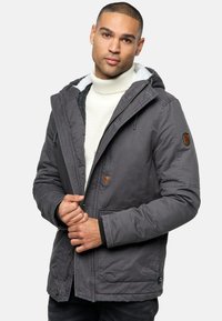 Grijze geïsoleerde jas met een capuchon, voorzien van een fleece-gevoerde kraag, een driehoekige accent en voorkruiszakken; de stof is glad met een matte afwerking.