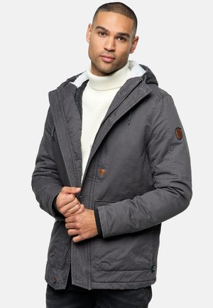 Chaqueta gris aislante con capucha, que presenta un cuello forrado de forro polar, un acento triangular y bolsillos frontales; la tela es suave con un acabado mate.