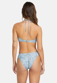 Modrý bikiny set s vzorom, ktorý obsahuje halterkrk top s viazaním a zodpovedajúce nízkopásové nohavičky, obe s intricátne bielymi vzormi.