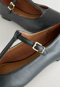 Černé kožené baleríny Mary Jane s tenkým páskem a zlatou sponou, kulatou špičkou a hnědou polstrovanou vnitřní podšívkou.