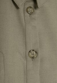 Khaki koszula z guzikami, wyróżniająca się teksturowanym materiałem, klasycznym kołnierzykiem i dwoma guzikami w pobliżu dekoltu, prezentująca gładkie i schludne wykończenie.