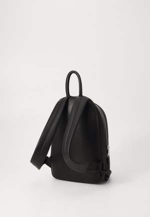 Mochila de cuero negro con un diseño redondeado, correas planas y un asa en la parte superior. Presenta un cierre de cremallera plateada en un lado para acceso y cierre.