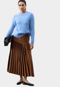 Světle modrý nadýchaný svetr, hnědá plisovaná sukně a černé balerínky. Plisé vytváří texturu a pohyb; jednoduchý, elegantní design oděvu.