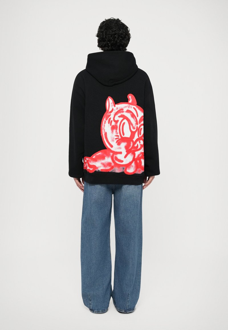 Svart hoodie med stort rött tecknat motiv på ryggen, kombinerad med lösa blå jeans. Har en avslappnad passform och en huva med dragsko.