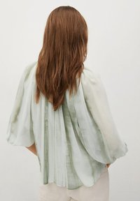 Blusa leggera in morbidi toni di verde e bianco; presenta un tessuto fluido, maniche a pipistrello ampie e un design con pieghe sul retro.