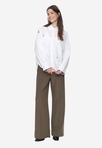 Biała koszula na guziki z kolorowymi haftowanymi wzorami, w połączeniu z luźnymi oliwkowozielonymi spodniami i czarnymi butami na bloczkowym obcasie.