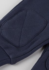 Dunkelblaues Textilkleidungsstück mit Ellbogenpatches und gesteppten Details. Weiches, strukturiertes Material mit gerippten Bündchen.