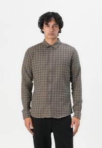 Brown checkered button-up shirt with a collar, long sleeves, and a relaxed fit. Made from a soft fabric with visible stitching details.