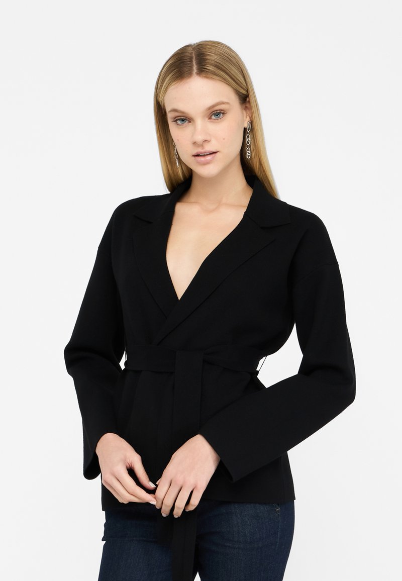 Sort indpakningsjakke med lange ærmer, notched krave og bælte i taljen. Glat tekstur, skræddersyet pasform og minimalistisk design.