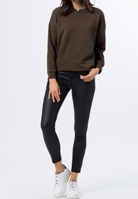 Olivgrön sweatshirt med avslappnad passform, rund halsringning och långa ärmar, kombinerad med svarta skinnybyxor och vita sneakers.