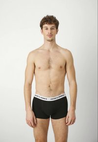 Černé boxerky s bílým páskem, na kterém je nápis "JACK & JONES." Materiál je hladký, design je přiléhavý s mírným vzestupem.