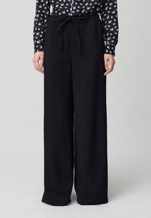 Pantalon large noir avec taille nouée, fabriqué en matériau doux. Caractéristiques d'une coupe décontractée et d'une légère texture, adapté à diverses occasions.