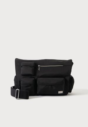 Sac bandoulière noir avec plusieurs poches zippées et à rabat, comprenant trois poches avant et une poche zippée supérieure, avec une sangle réglable.
