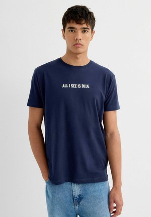 Camiseta de algodón azul marino de manga corta y cuello redondo, con texto blanco que dice "TODO LO QUE VEO ES AZUL" en el pecho.