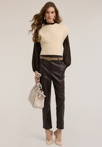Kremowy sweter z dzianiny o fakturowanym wzorze, na czarnej bluzce z długim rękawem, zestawiony z błyszczącymi ciemnymi spodniami, cielistymi szpilkami i beżową torebką.
