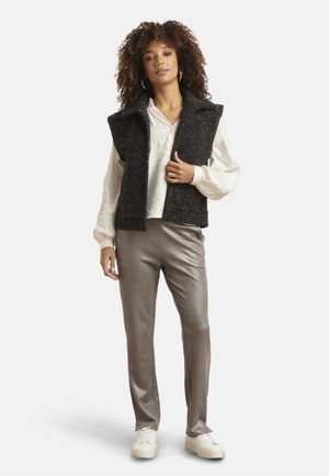 Ärmellose Weste aus schwarzem Wollmix über einer weißen Bluse, kombiniert mit glänzenden silbernen Hosen und weißen Sneakers. Schlichtes Design mit strukturiertem Finish.