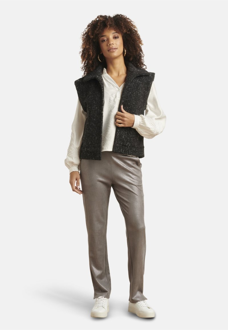 Ärmellose Weste aus schwarzem Wollmix über einer weißen Bluse, kombiniert mit glänzenden silbernen Hosen und weißen Sneakers. Schlichtes Design mit strukturiertem Finish.