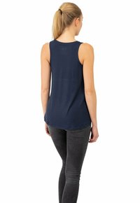 Dunkelblaues ärmelloses Tanktop mit abgerundetem Saum, weichem Material und tailliertem Design, kombiniert mit grauen Skinny Jeans.
