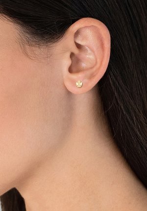 Boucles d'oreilles en or en forme d'ange unique, avec des surfaces lisses et une finition polie, exposées sur une oreille.