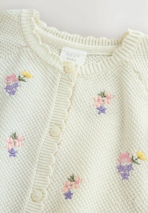 Gestrickte Babyjacke in Creme mit wellenförmigem Ausschnitt, verziert mit pastellfarbenen Blumenstickereien und Knopfverschluss vorne. Weiche Textur.