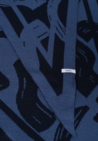 Strikket tørklæde i mørkeblå og marineblå med et grafisk design. Mærke synligt med navnet "CECIL" på en hvid lap.