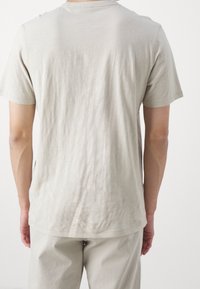 Helles beiges T-Shirt mit kurzen Ärmeln, aus weichem Stoff und lockerem Schnitt. Glatte Textur mit einem schlichten Design, ohne Muster oder Grafiken.