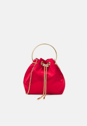Rød satin håndtaske med snorelukning, guldfarvet metalring som håndtag og kæderem mod en ensartet lys baggrund.