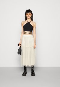Top halter preto cropped com alças cruzadas, combinado com uma saia de tule em camadas ivory, botas de combate pretas e uma pequena bolsa preta.