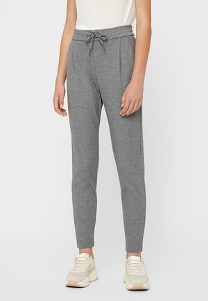 Pantalon de survêtement gris avec une taille élastique et un cordon de serrage, comportant des plis subtils et des jambes fuselées. Associé à des baskets de couleur claire.