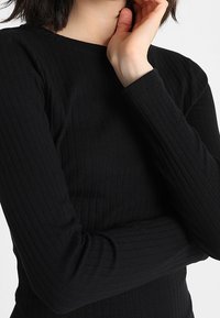 Czarny prążkowany top z długim rękawem i okrągłym dekoltem. Tkanina ma miękką fakturę i posiada pionowe paski. Slim-fit design.