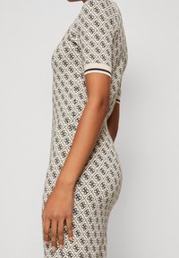 Robe en tricot crème avec un motif en diamant et des accents foncés, dotée de manches courtes et d'une silhouette ajustée.